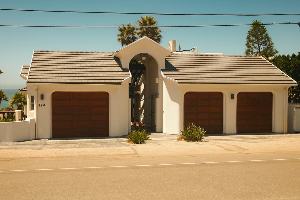 A stucco house with three wood-look sectional garage doors and palm trees behind