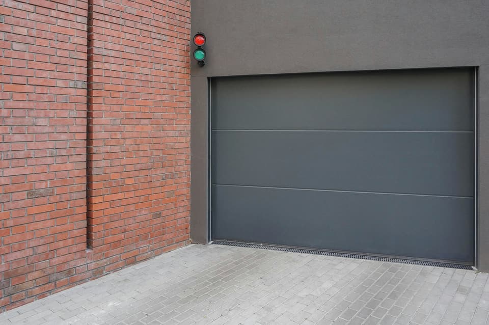 A flush grey sectional garage door beside a brick wall