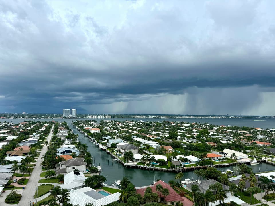 A dark storm cell over a canal-front neighbourhood with rain falling in the distance