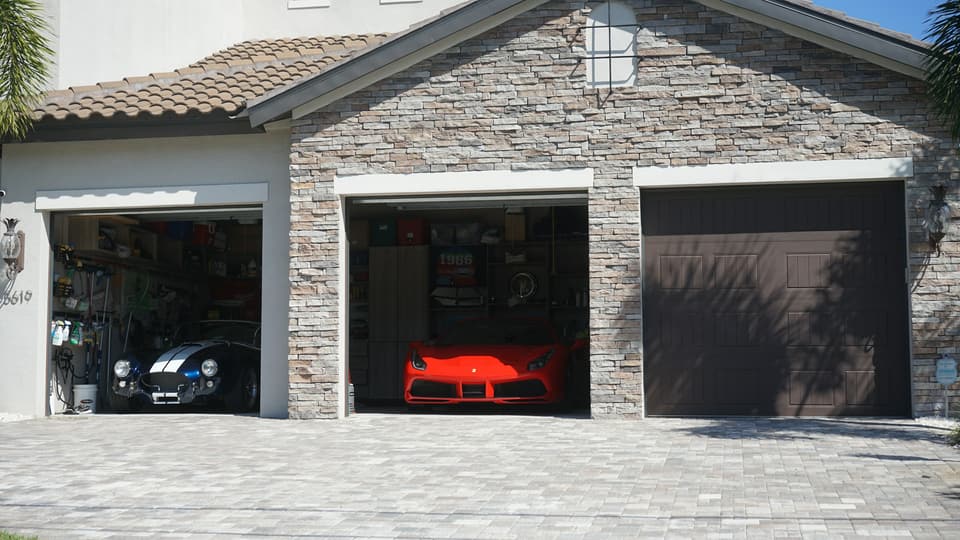 A three-bay garage with two doors open and one dark brown door closed, above a paver driveway