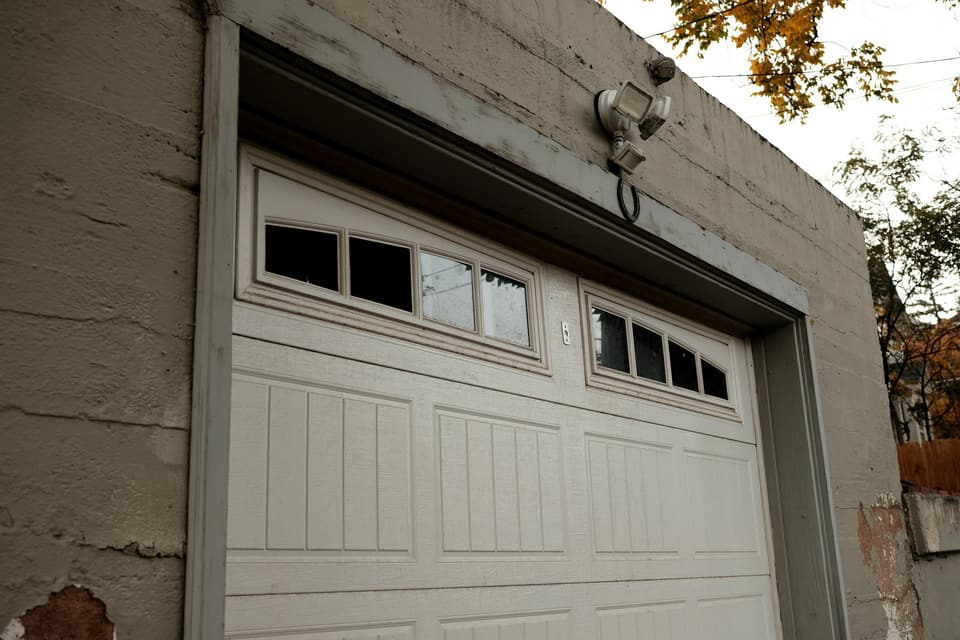 An older white sectional garage door with a row of windows, set in a weathered concrete wall